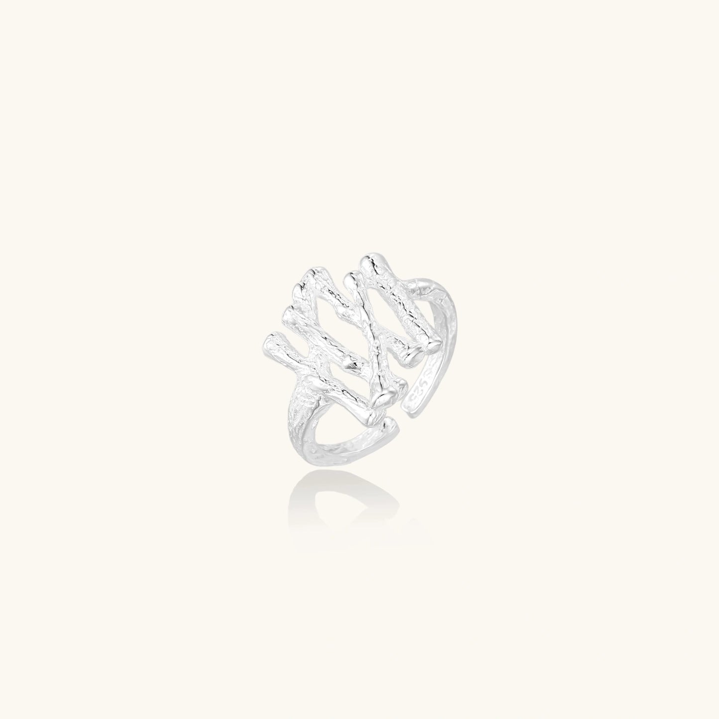 Sculptural sterling silver ring with organic branch design and textured surfaces on cream background