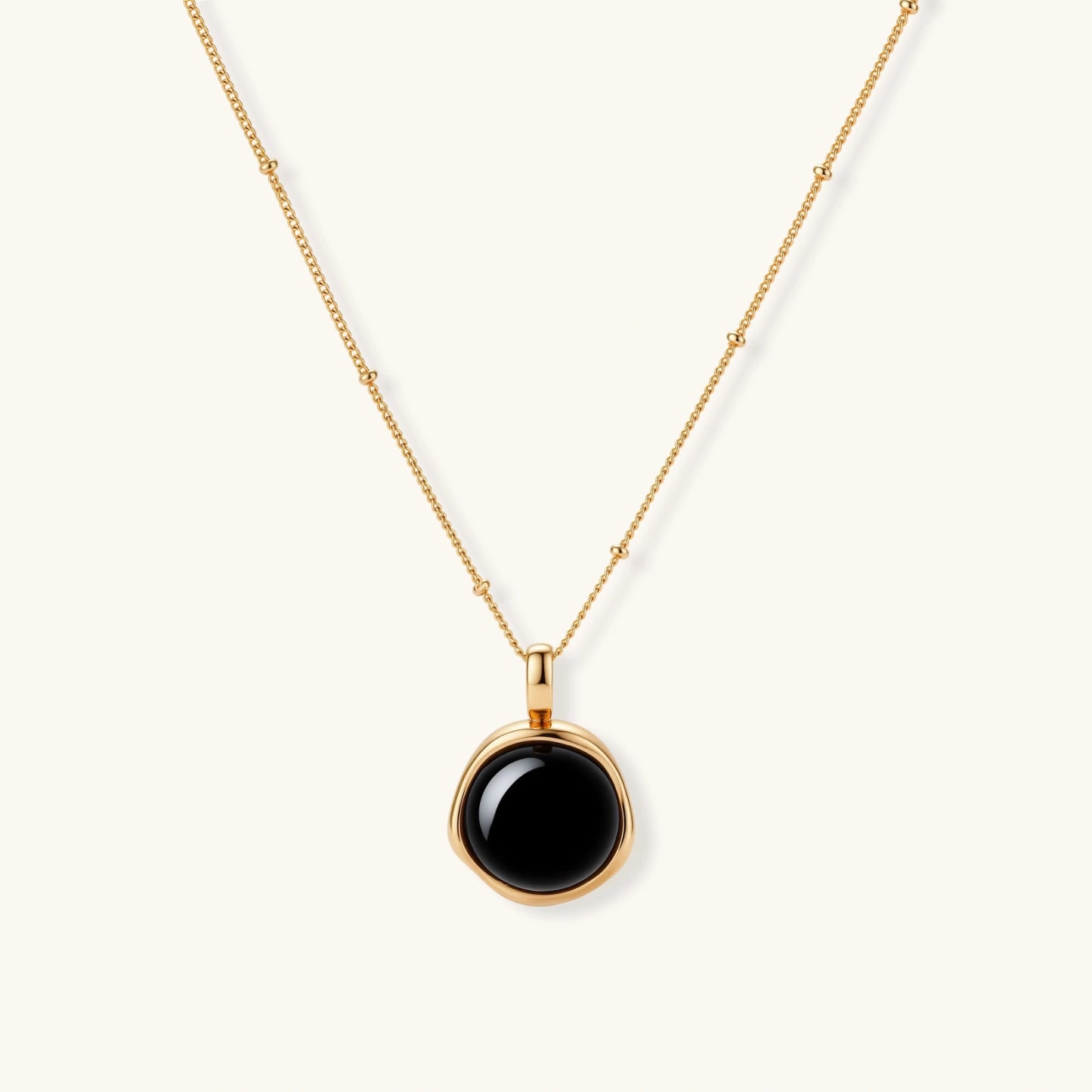 Circular black agate pendant on gold-plated sterling silver chain against cream background, showing modern minimalist design.