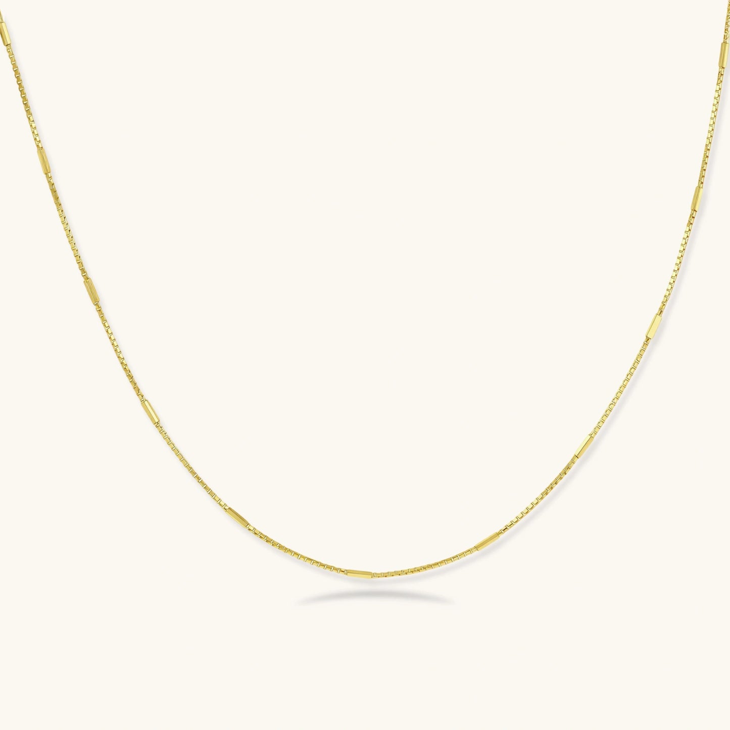 Delicate 14K gold-plated box chain necklace with evenly spaced bar links, shown flat on cream background.